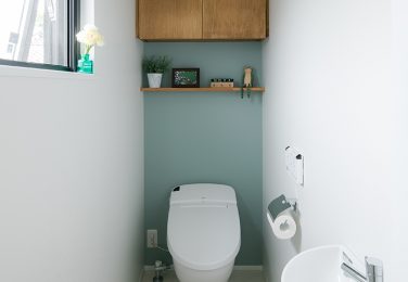 淡いブルーのアクセントクロスに収納と飾り棚のあるトイレ