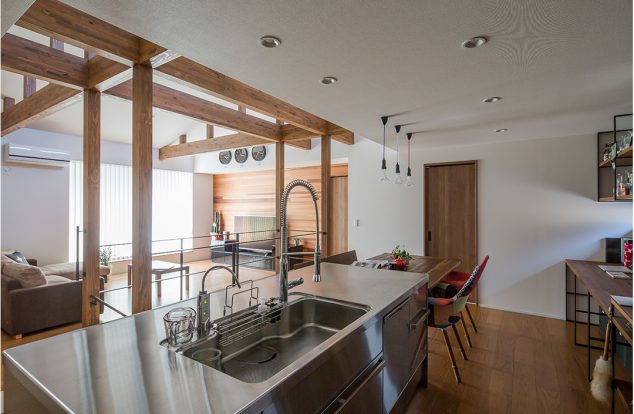 梁の見えるリビングを見渡せるステンレスのキッチン