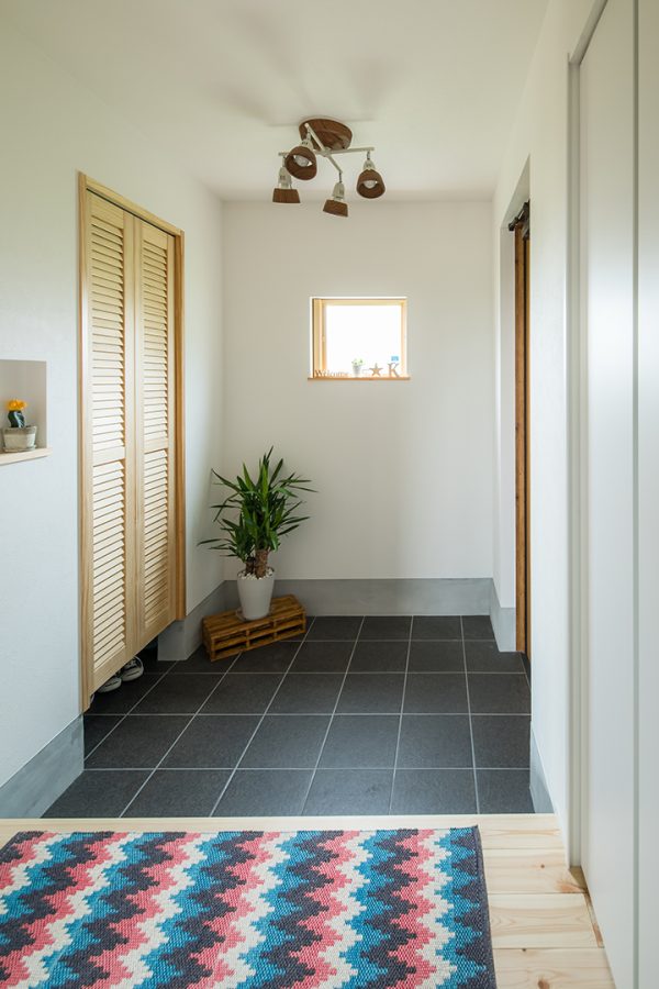 濃い色のタイルで正方形の小窓のある玄関　