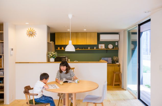 緑のアクセントクロスに明るい木目のキッチンの見えるカジュアルなダイニング　