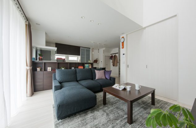 大きな吹抜けから光が注ぐ、白ベースに落ち着いた色目でコーディネートされたリビング　