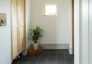 濃い色のタイルで正方形の小窓のある玄関　
